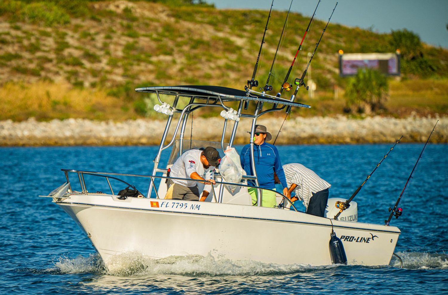 Fishing boat with passengers and equipment cruising on bright blue waters near rocky coastline.