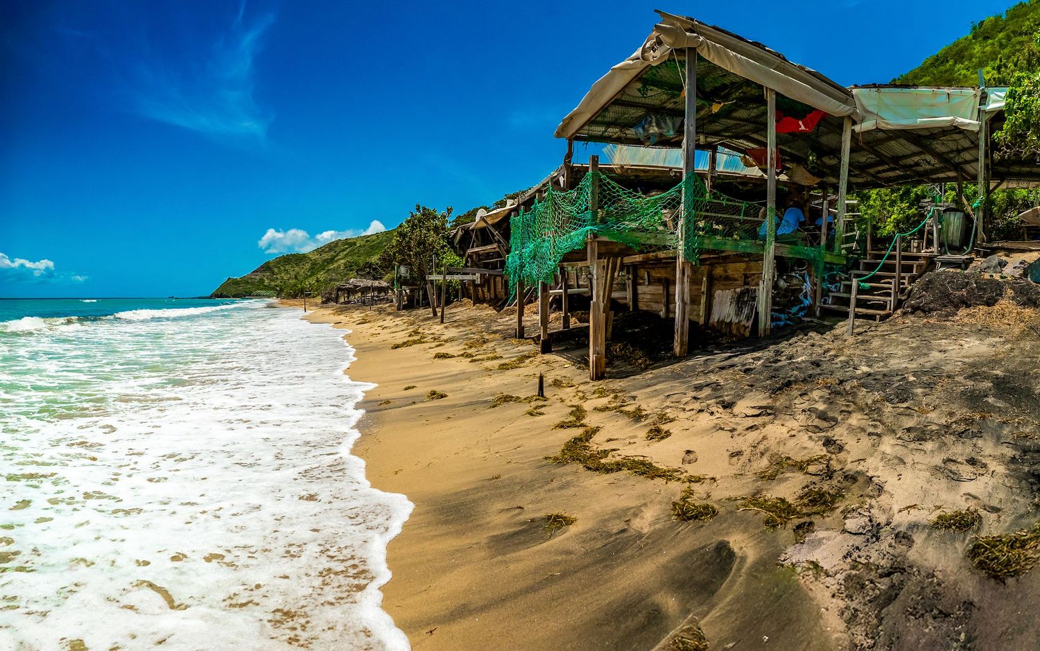 Panoramic view of a tropical beach with white sand and turquoise waters against a bright blue sky.