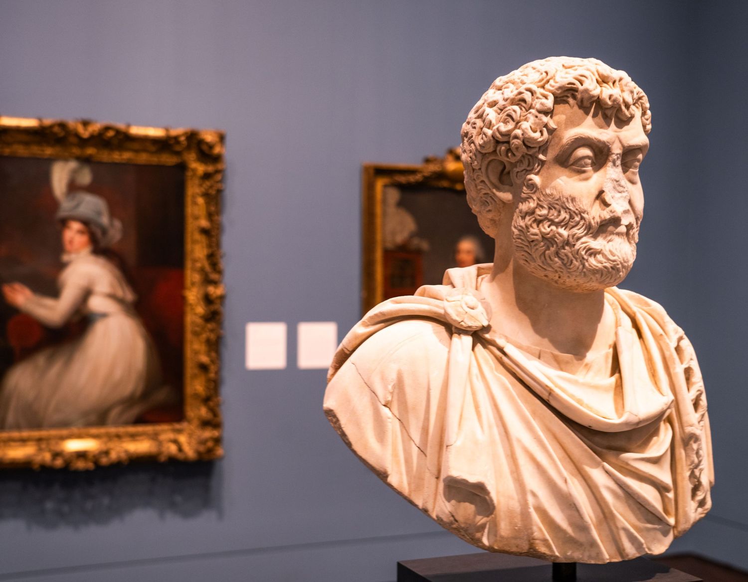 Classical sculptures and artworks displayed in a museum gallery with blue walls.