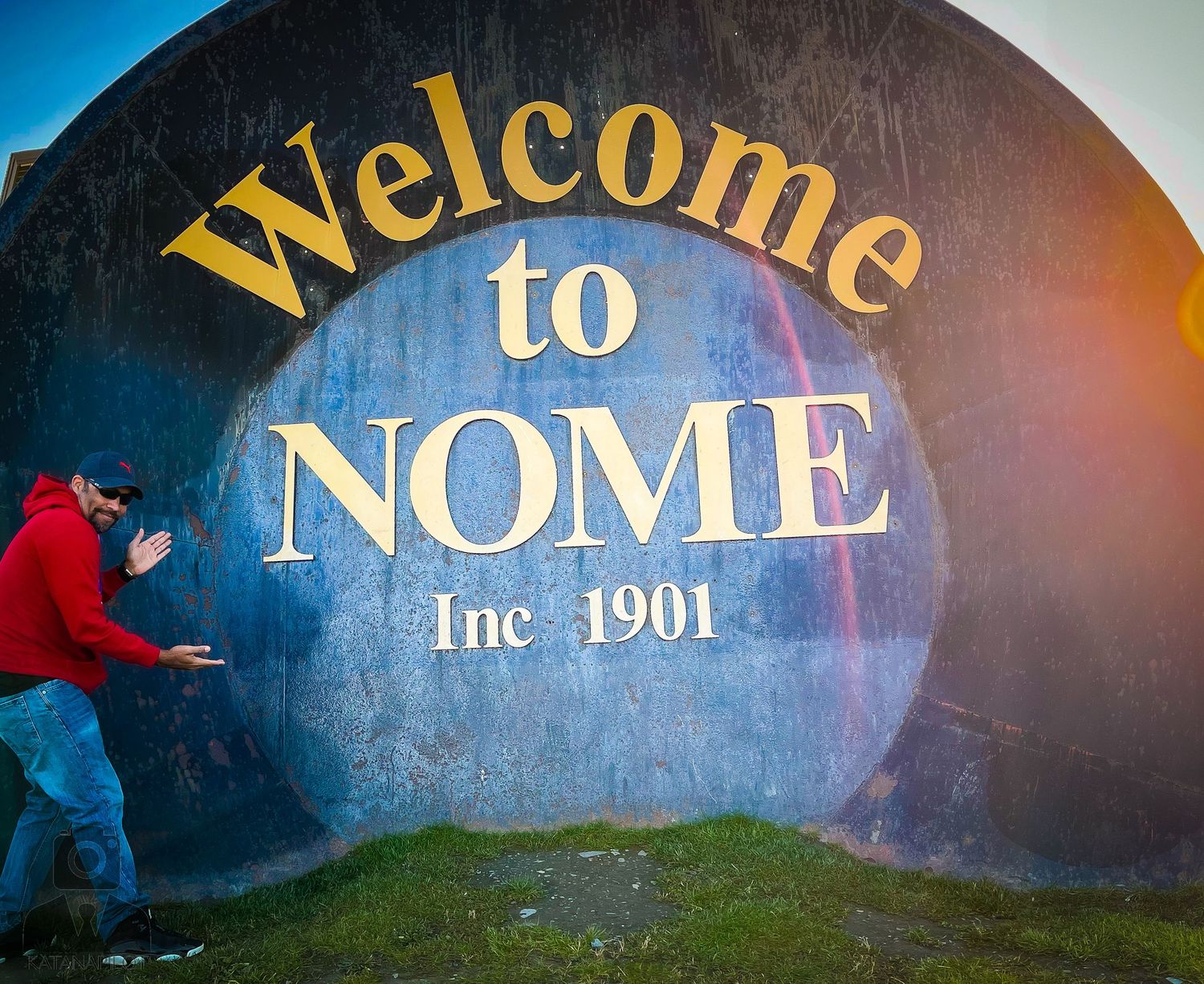 Welcome sign for Nome city illuminated at dusk with golden lettering against a dark sky.