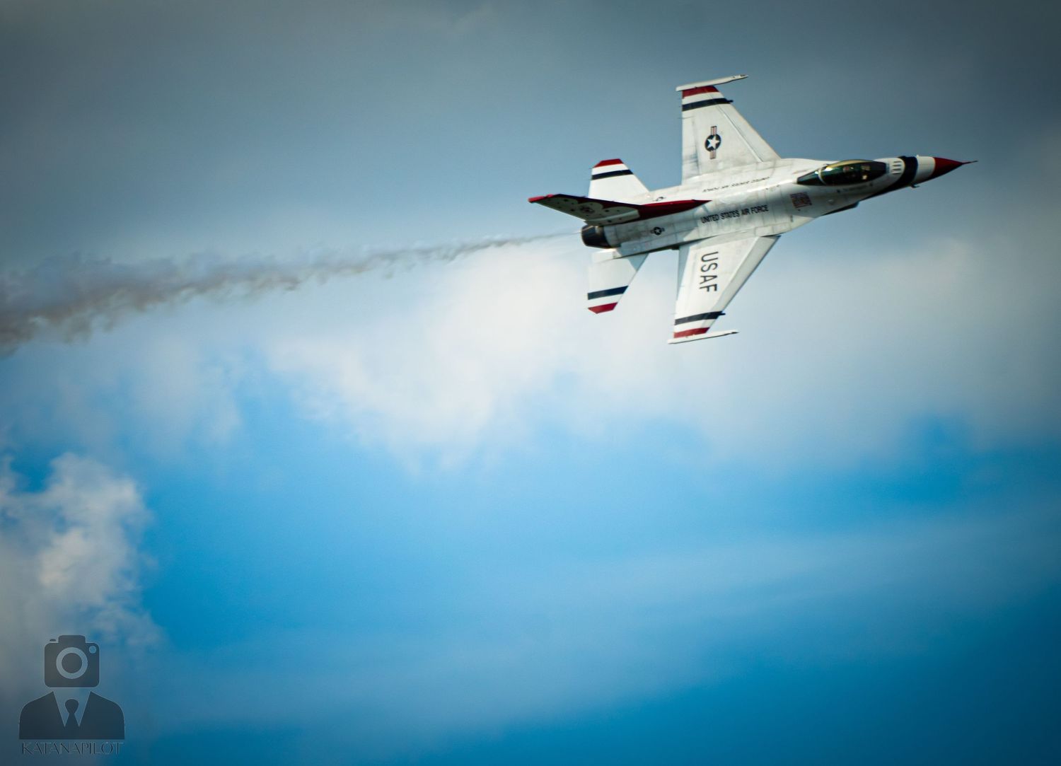 USAF Thunderbirds jet performs aerial maneuver leaving white smoke trail against blue sky at airshow.