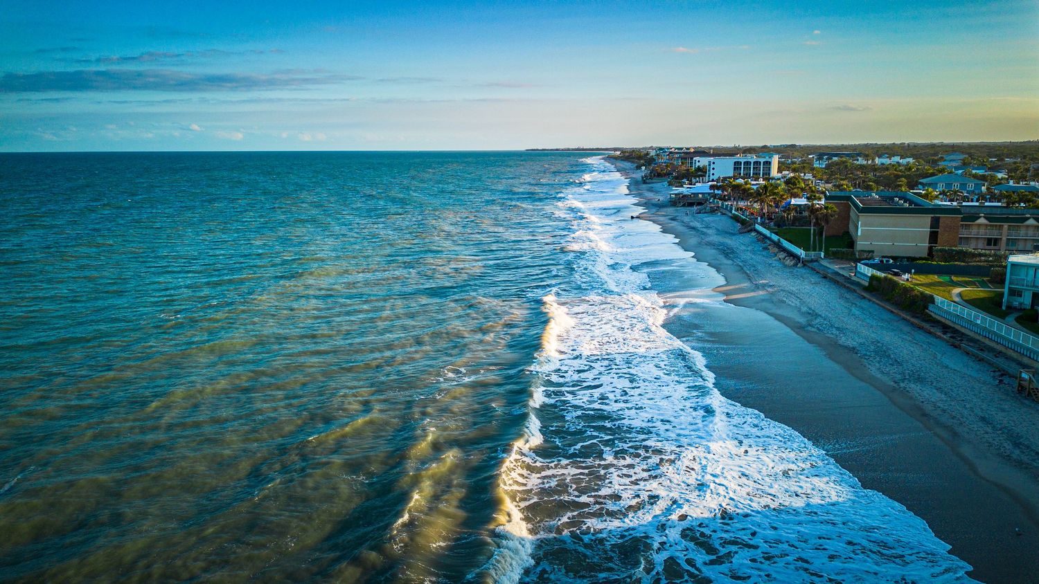 Aerial view of a pristine coastline with turquoise waters and beachfront properties during golden hour.