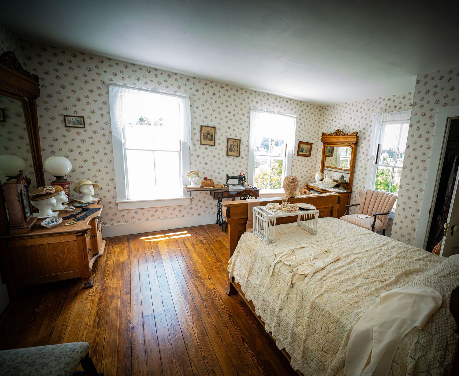 Spacious bedroom with floral wallpaper, hardwood floors, and antique wooden furniture.