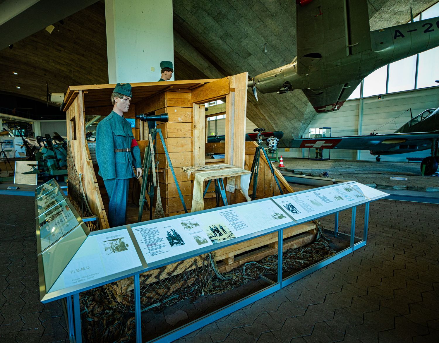 Museum exhibit of a uniformed soldier mannequin beside a wooden observation tower with an informational display and vintage aircraft nearby.