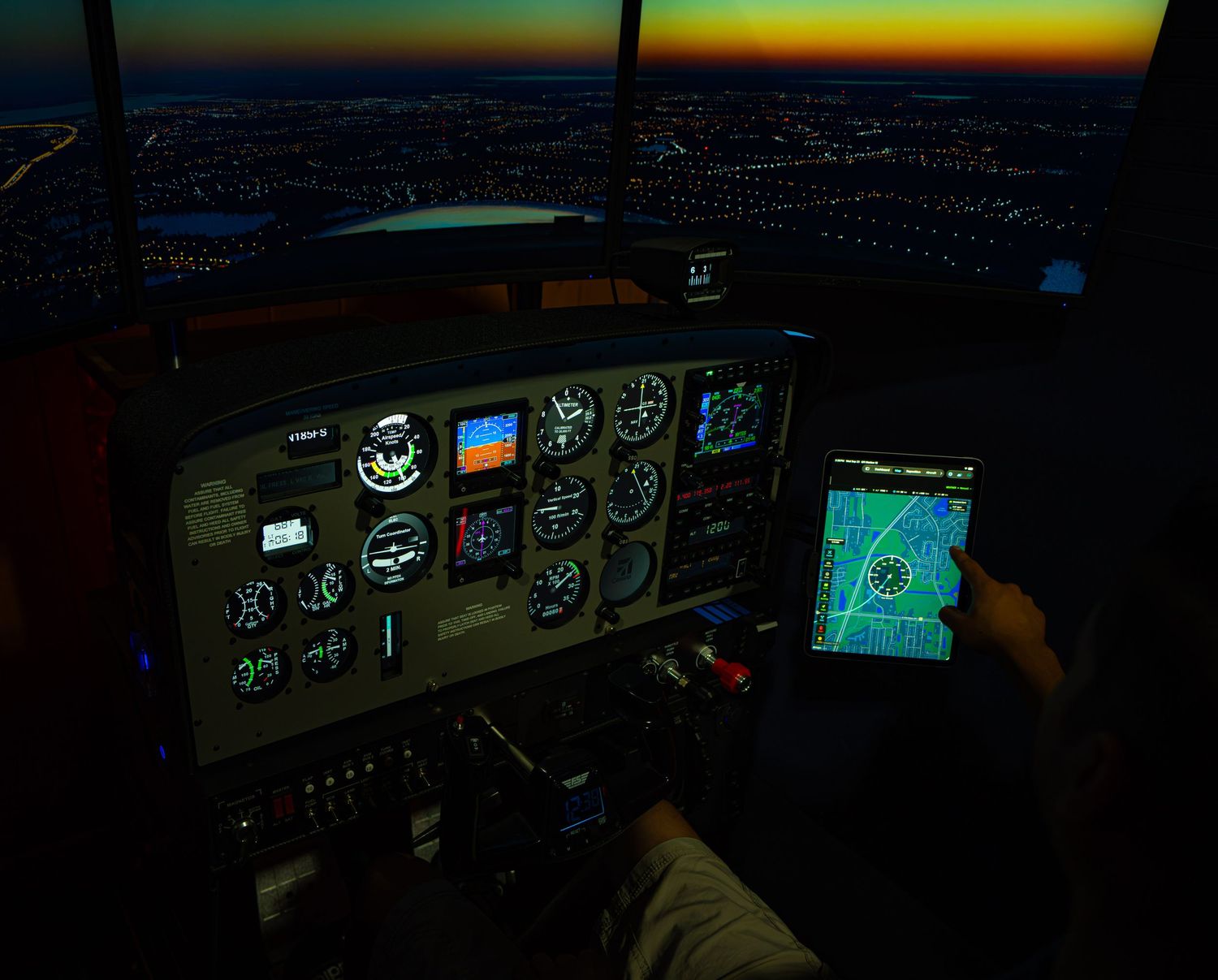 Pilot cockpit view at dusk with illuminated flight instruments and GPS navigation display over city lights.