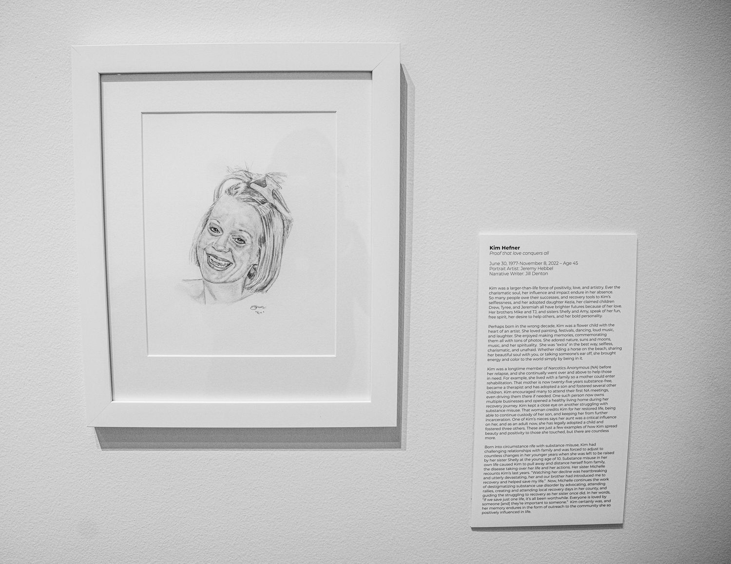 Gallery exhibition showing pencil portrait sketches with corresponding written narratives.