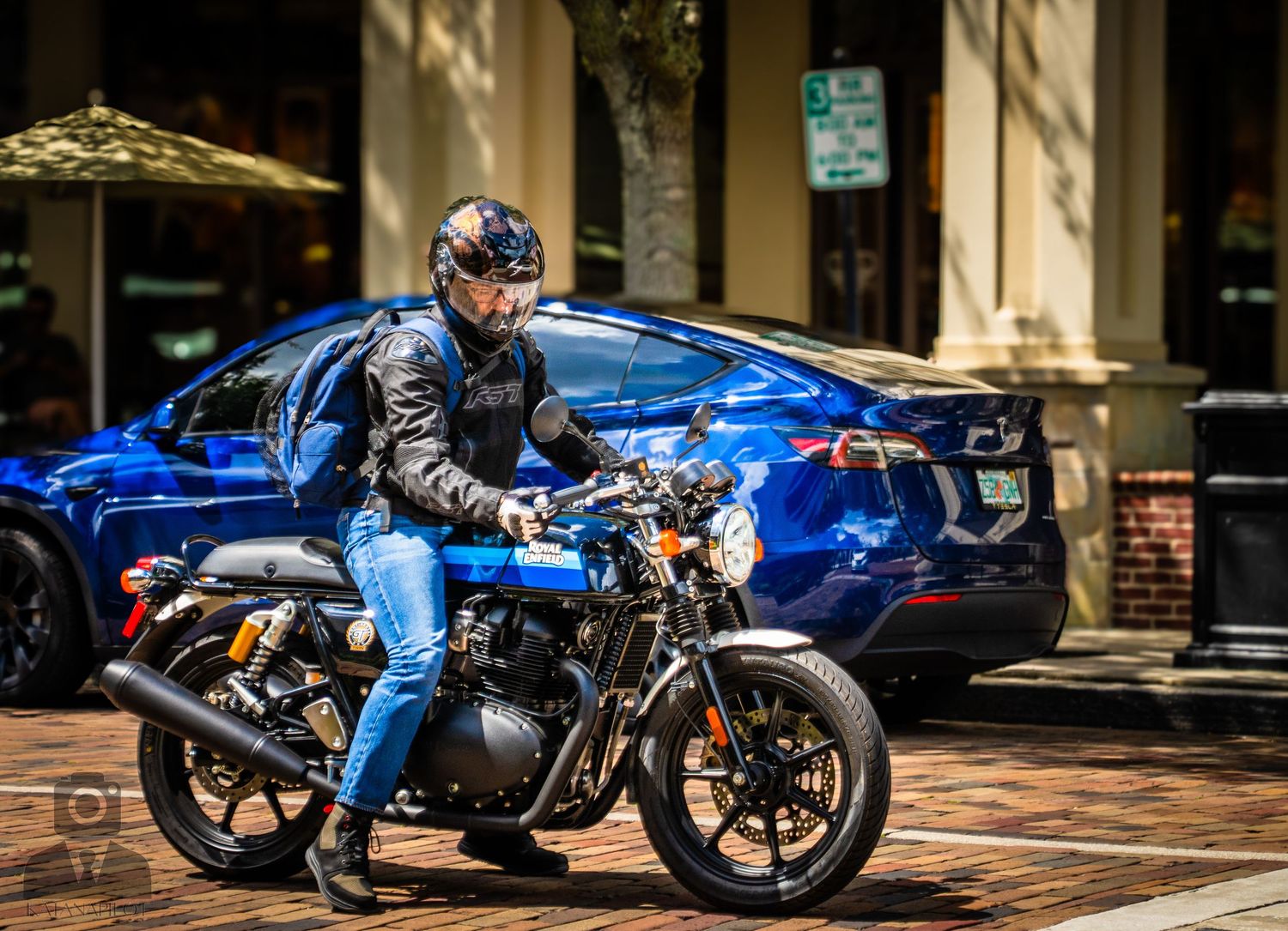 A bright blue vintage motorcycle is parked in front of a brick building with arched windows.
