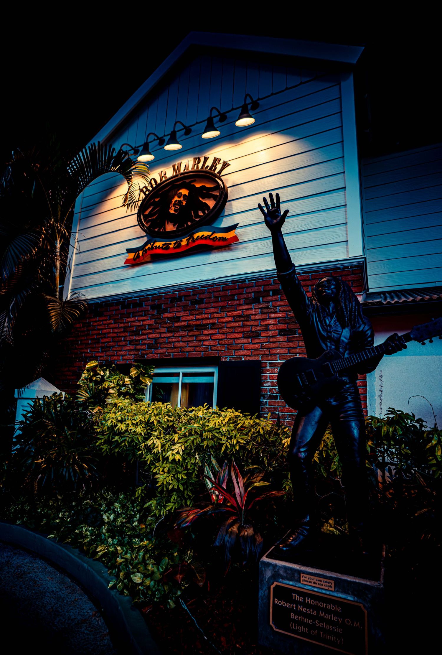 A dark exterior shot of a restaurant with illuminated signage and a decorative statue silhouetted against a brick wall.