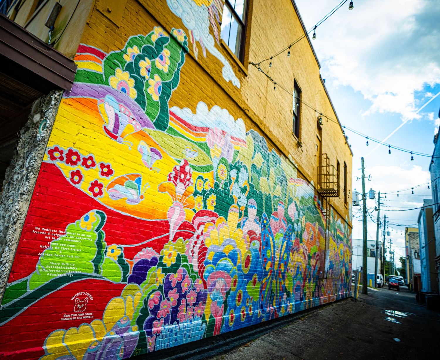 Colorful street art murals with vibrant abstract designs cover long walls along an urban alleyway.