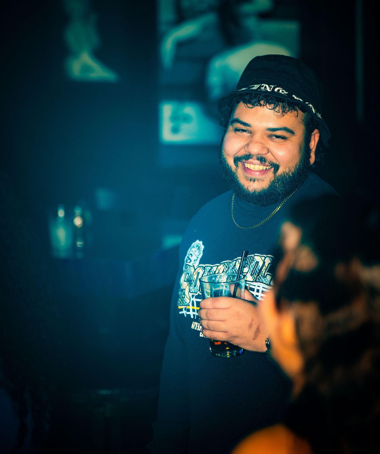 Smiling DJ in casual attire performing at a nightclub with blue ambient lighting.