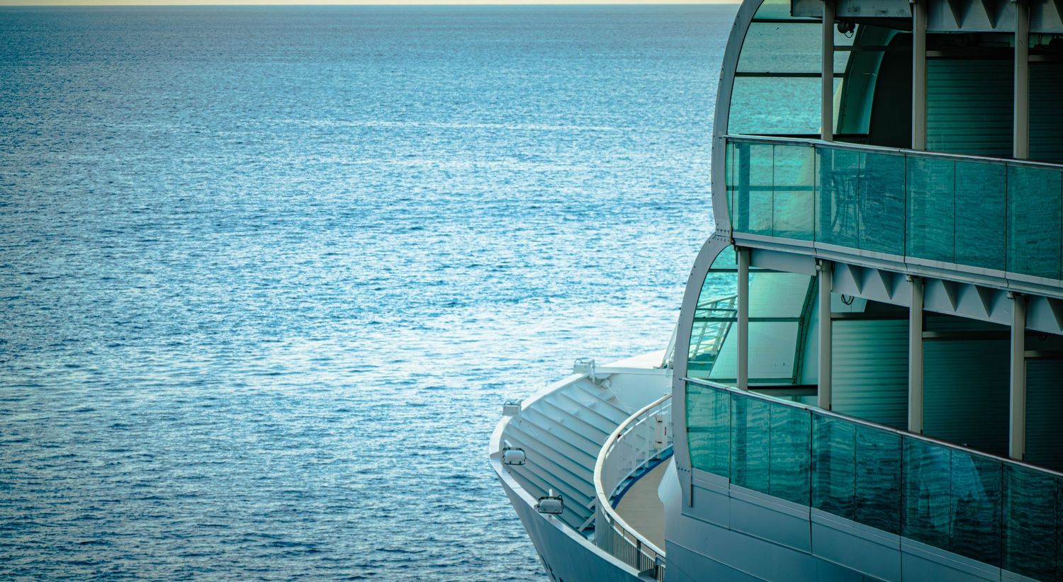 A luxurious cruise ship balcony overlooks the calm blue ocean waters on a sunny day.