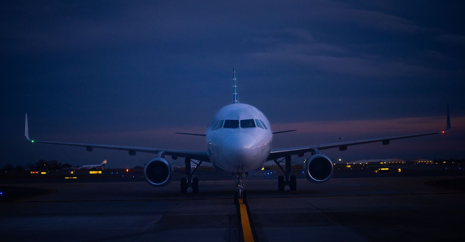 Commercial passenger jet aircraft silhouetted against dramatic sunset sky at airport with orange and purple hues.