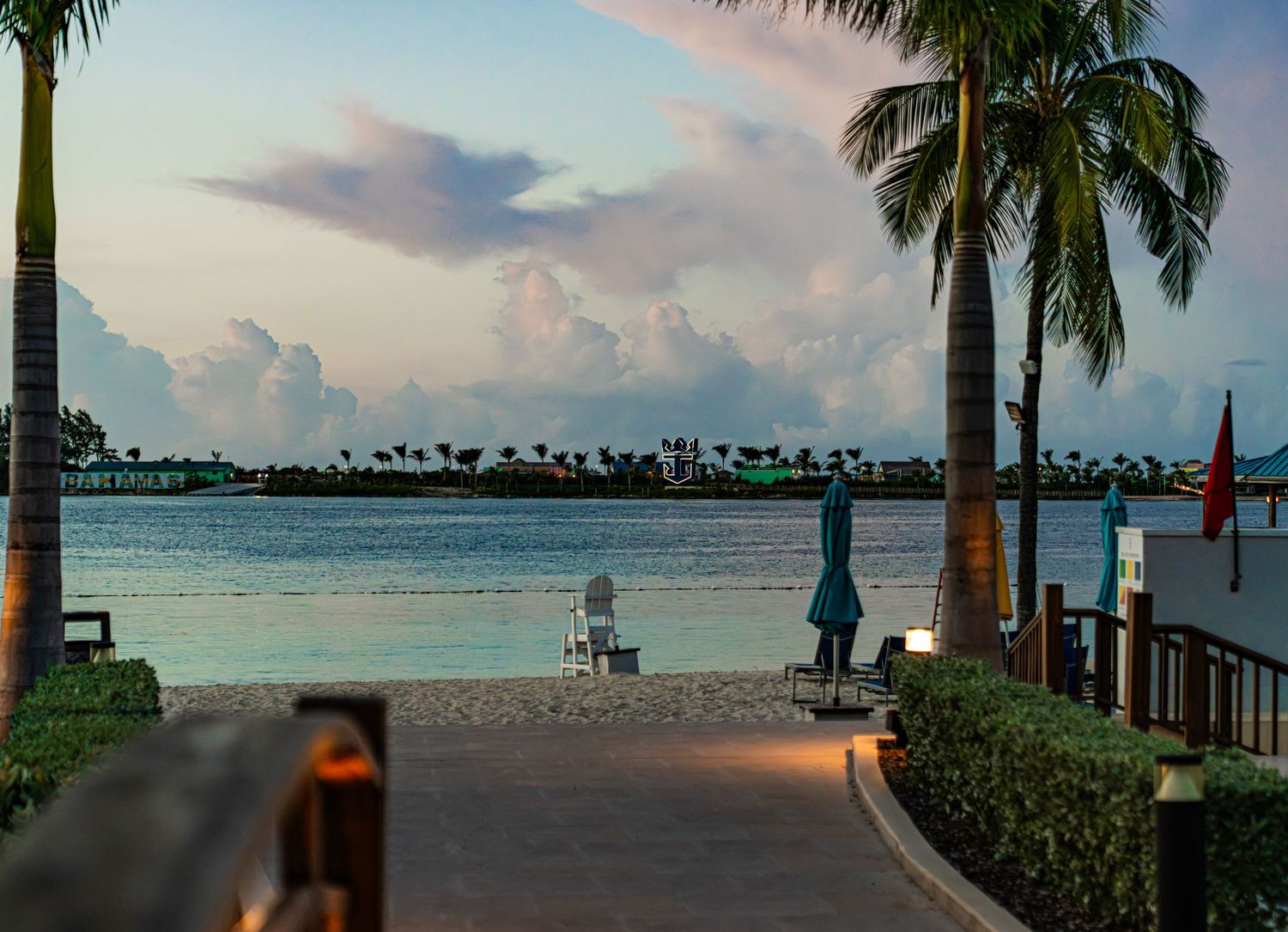 Serene tropical beach at dusk with palm trees, lounge chairs, and calm turquoise waters under a pastel sky.