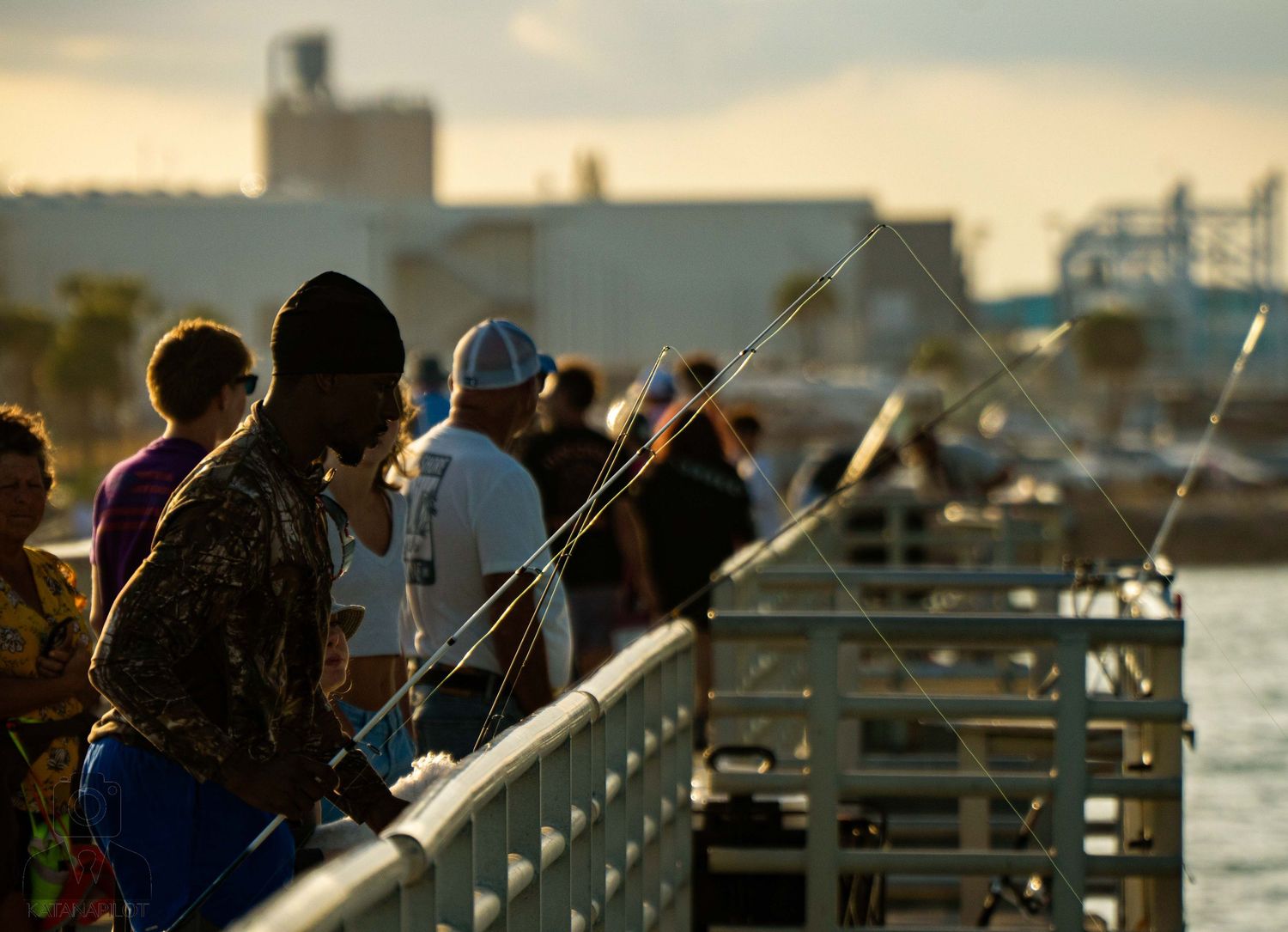 People gather along a railing at sunset to watch boats on the water below.