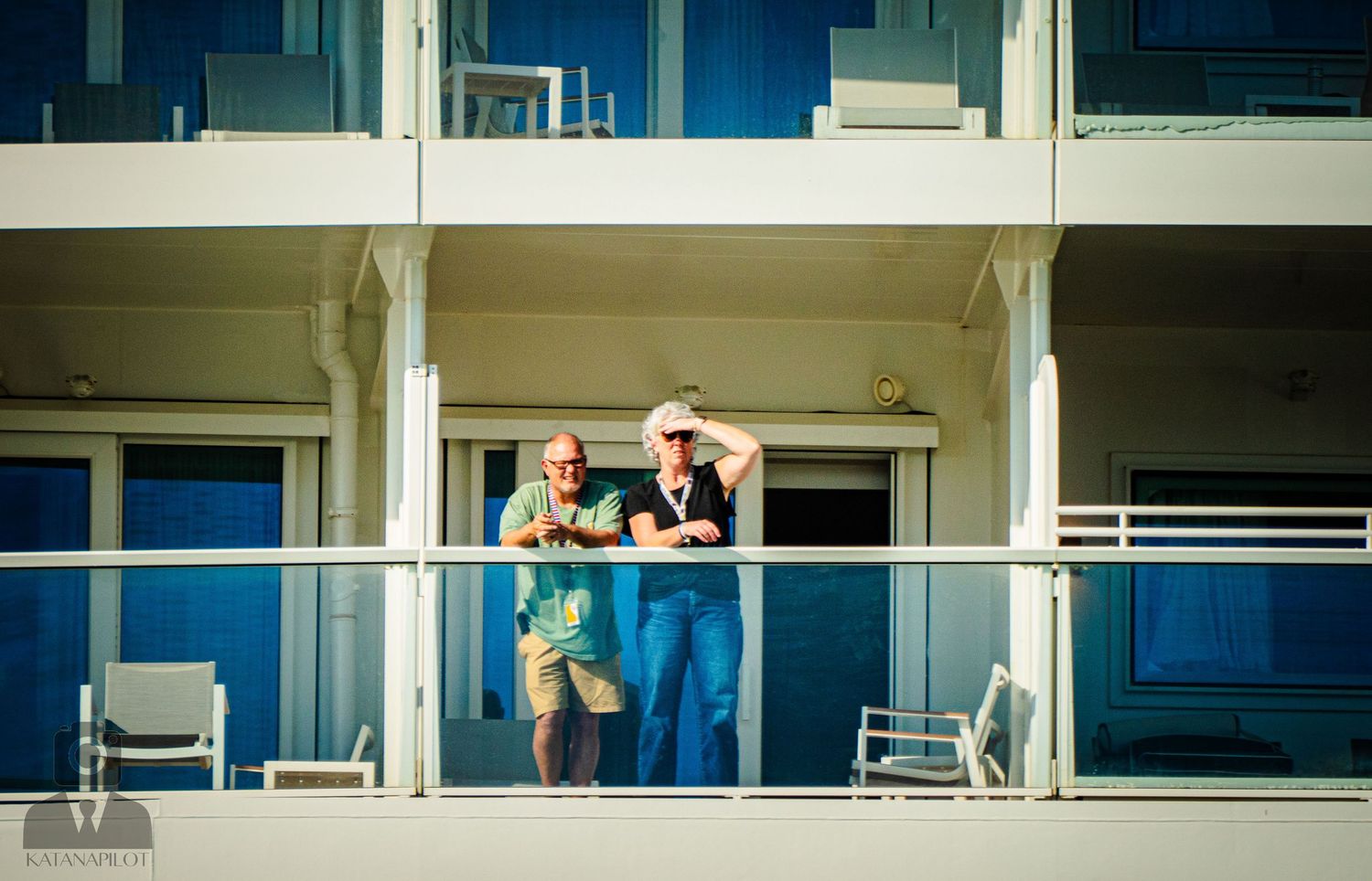 People gather on multiple balconies of a modern building with glass windows and white railings.