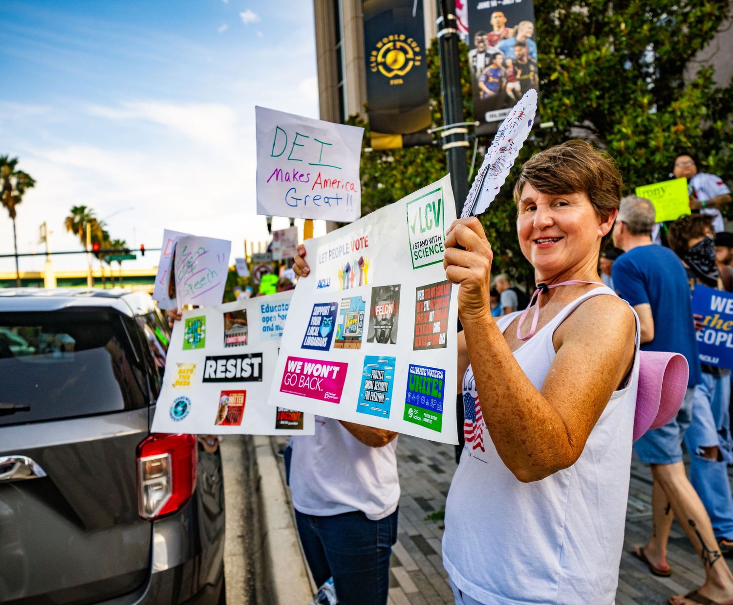 Demonstrator holds up multiple protest signs at an outdoor rally.