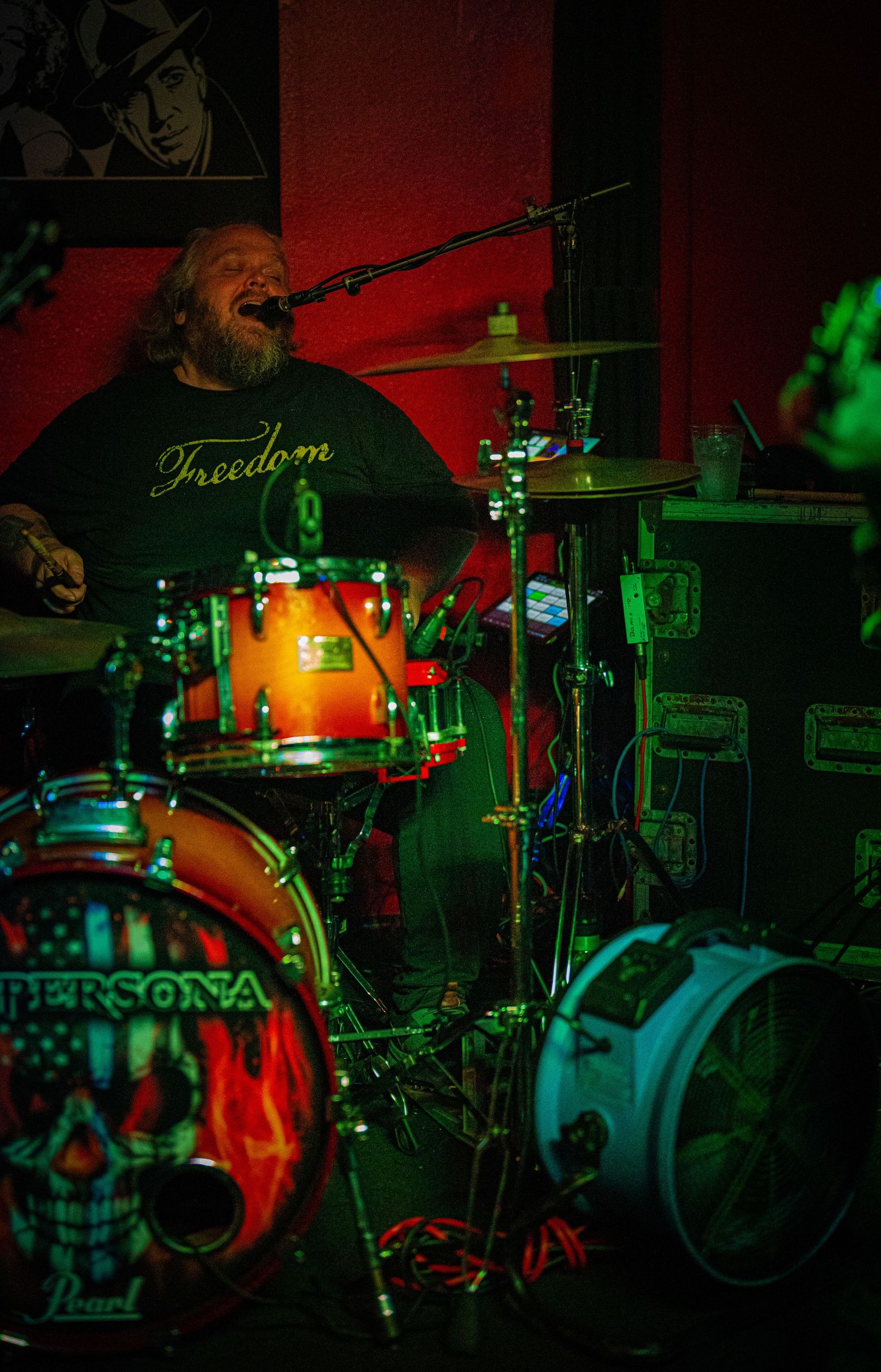 Drum kit setup with 'Freedom' branding visible under mixed red and green stage lighting.