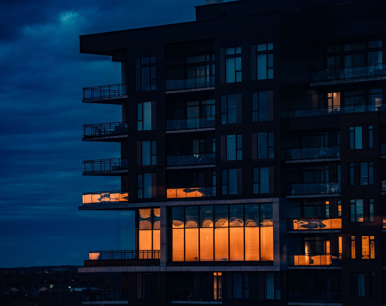 Apartment building silhouette at dusk with warm glowing windows.