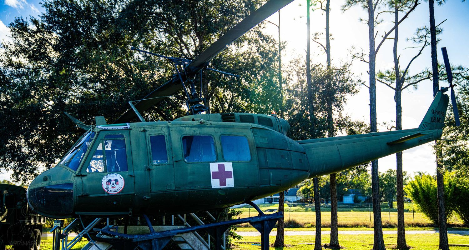 Military rescue helicopter with medical cross markings displayed among trees at an outdoor museum.