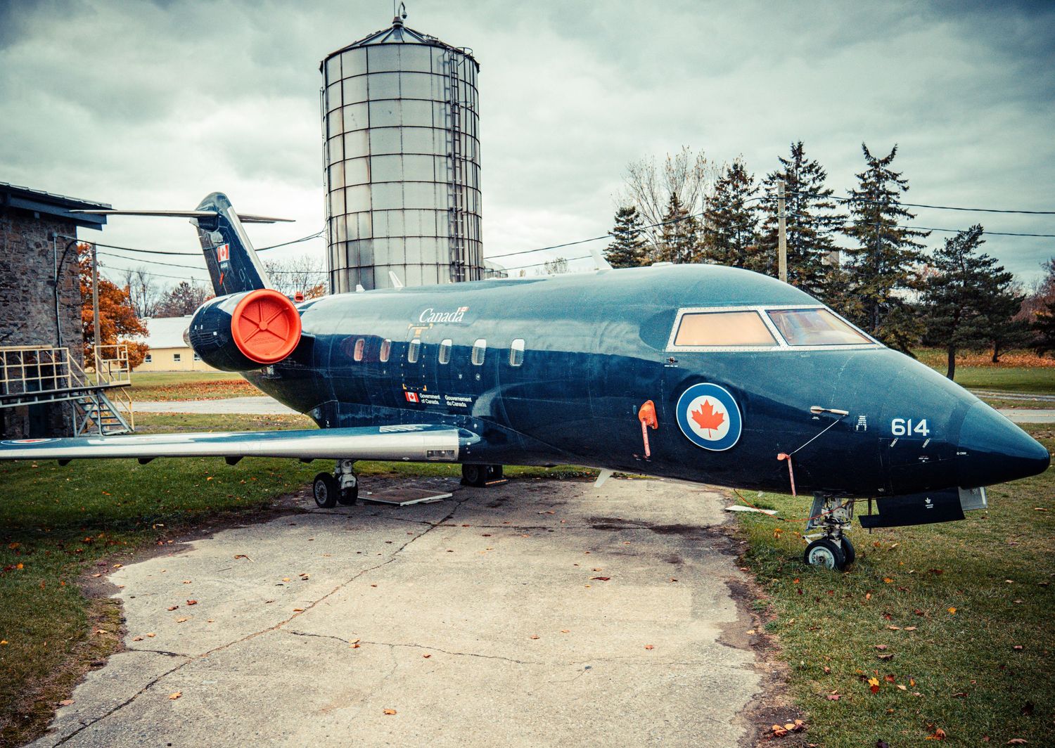 Military aircraft parked near industrial silos under cloudy skies.