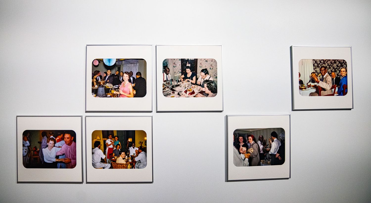 Row of framed photographs displayed on a white gallery wall showing various scenes and moments.