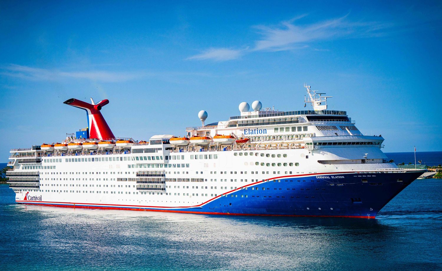 Carnival cruise ship sailing on calm blue waters under a bright clear sky.