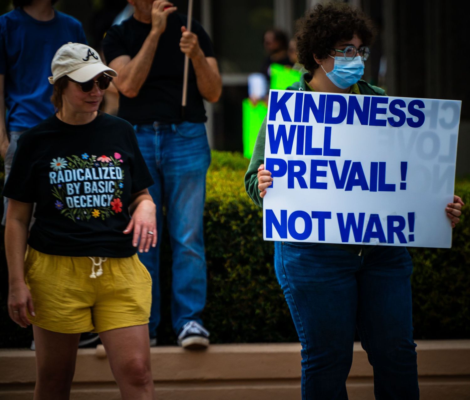 Protesters hold signs advocating for peace and kindness during a street demonstration.