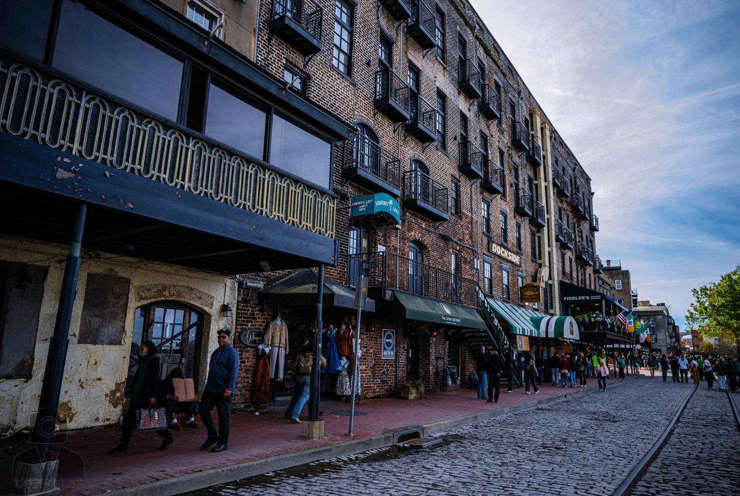 Historic brick buildings line both sides of a cobblestone street in a charming downtown district.