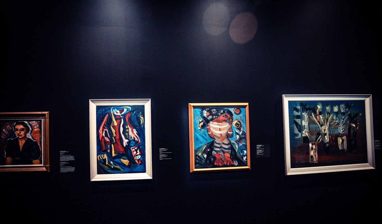 Row of illuminated photographs displayed against dark walls in museum gallery setting.