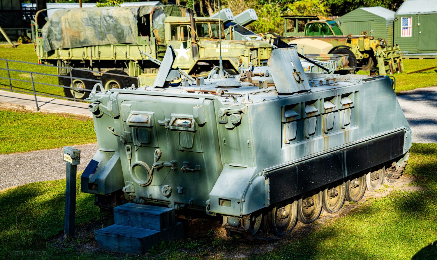 Row of vintage military vehicles and armored personnel carriers on display in a grassy field.