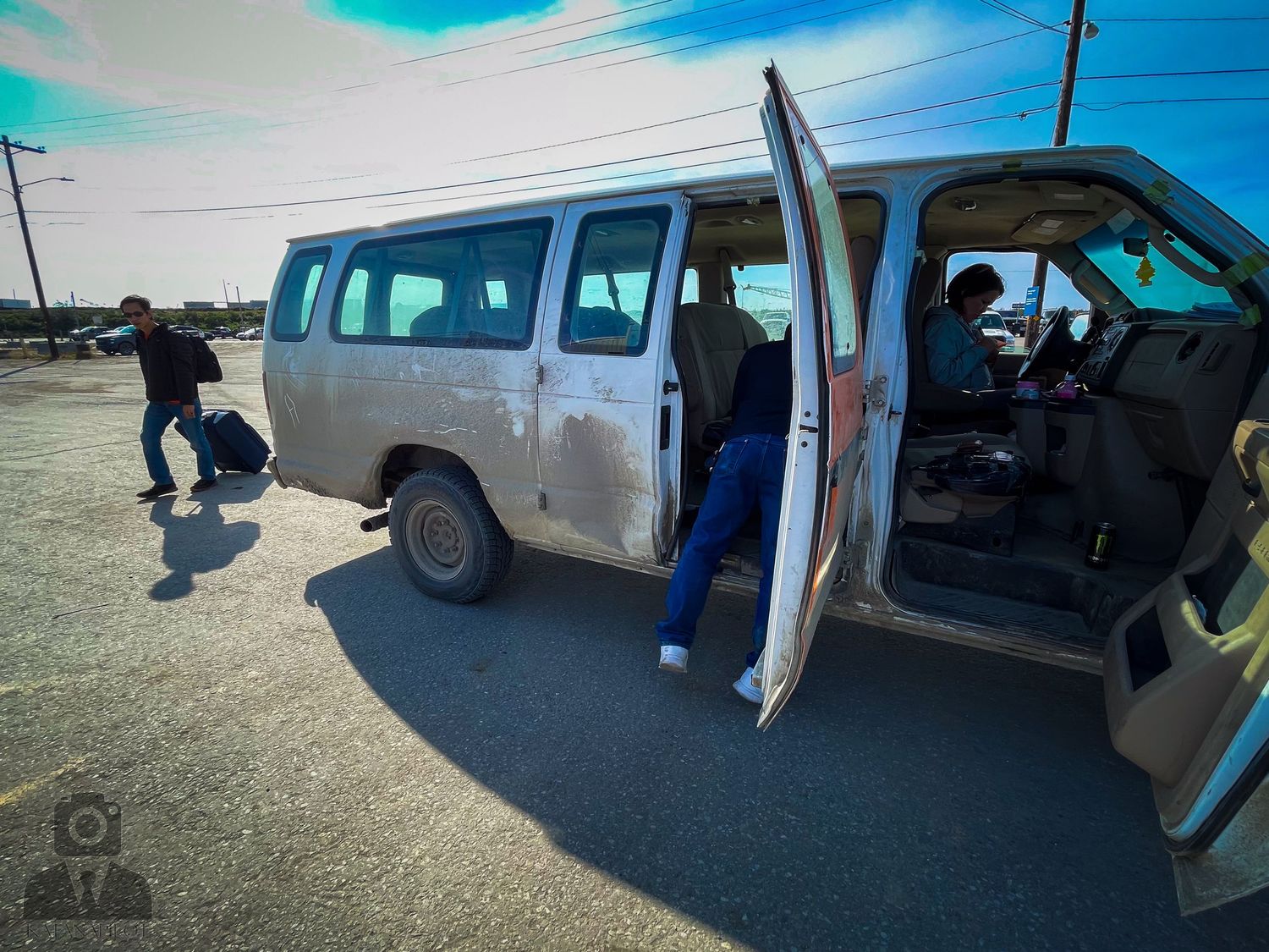 Surfboards strapped to the roof of a parked van against a bright blue sky.
