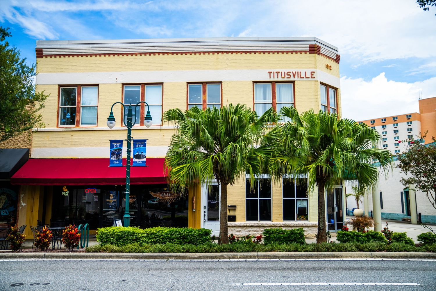 Series of beige commercial buildings with large windows and palm trees in a shopping district.