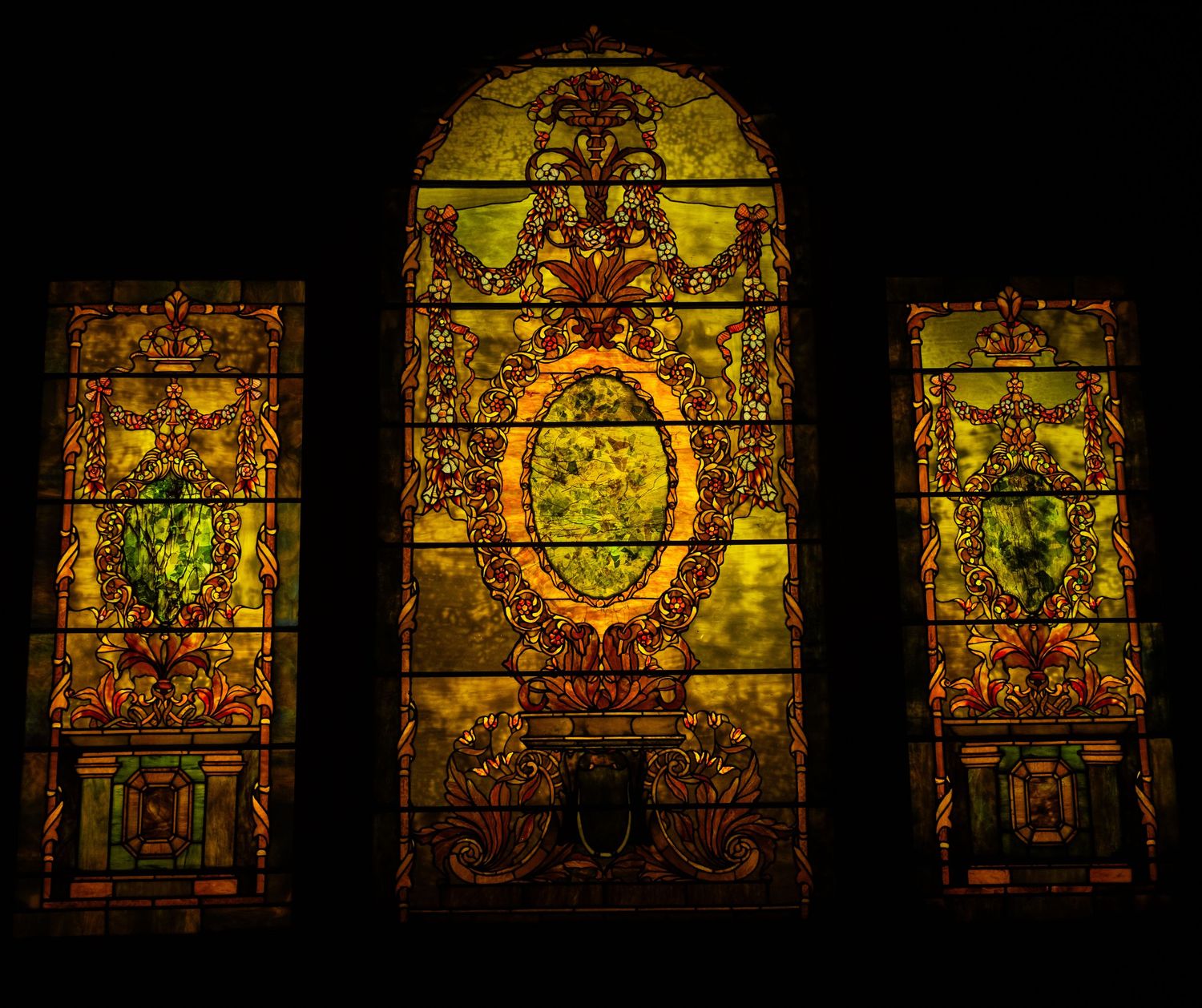 Three ornate stained glass panels with golden yellow tones featuring decorative Victorian patterns.