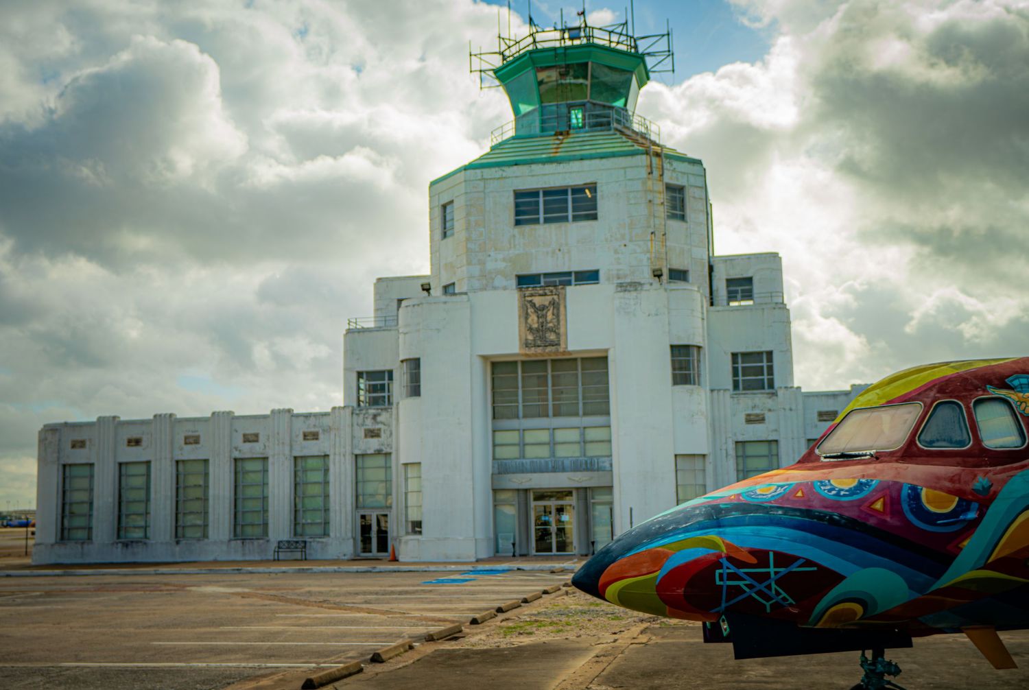 Art deco airport control tower with colorful painted aircraft on tarmac under dramatic cloudy sky.