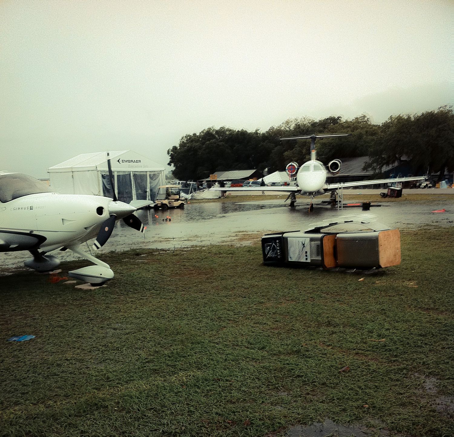 Several small aircraft parked on a grassy field during overcast weather with dark storm clouds in the background.