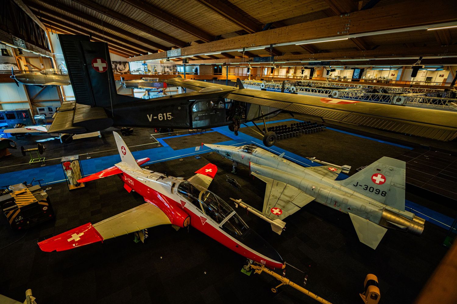 Swiss Air Force jets with red and white livery on display inside an aviation museum hangar, with more aircraft suspended from the ceiling.
