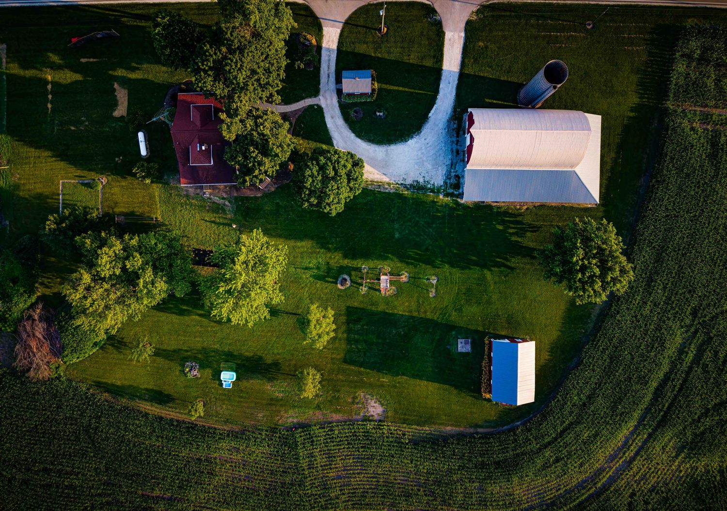 Aerial view of a rural farm property with green fields, trees, barns, and outbuildings on a sunny day.