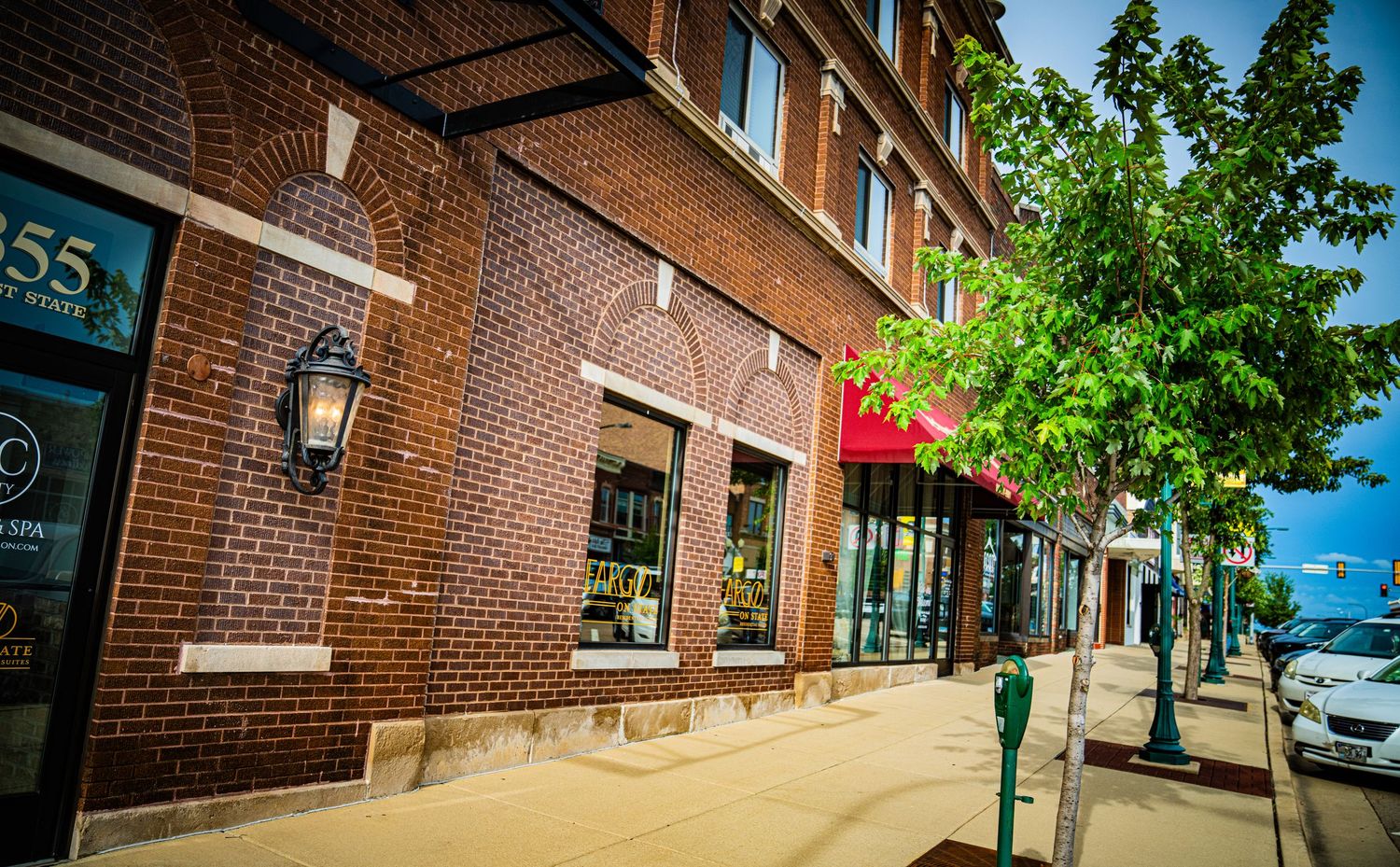 Red brick storefront buildings with classic architecture and tree-lined sidewalk.