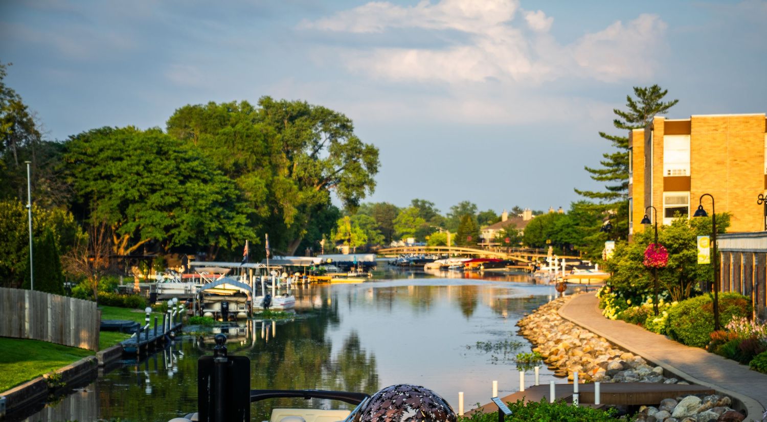 Panoramic view of a lakeside walkway with metal sculptures and docks during golden hour.