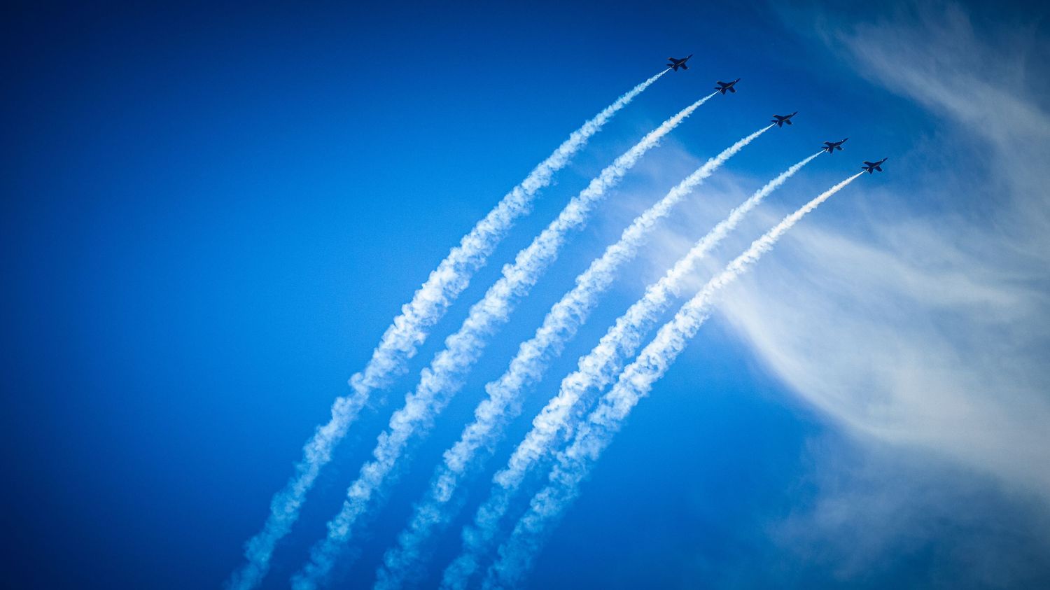 Five parallel contrails streak across blue sky during aerial demonstration.