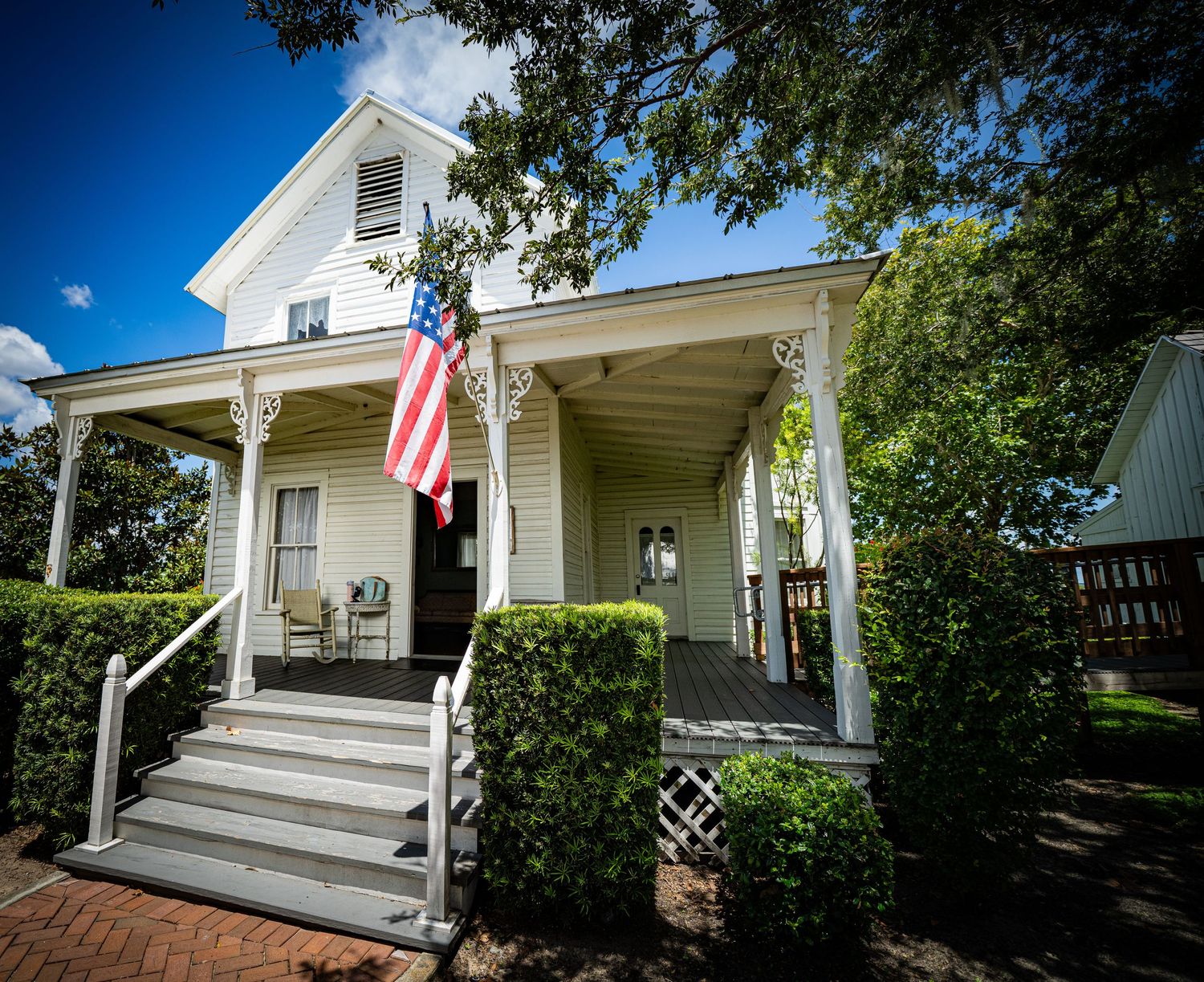 White historic house with American flag and wraparound porch featuring classical architectural details.