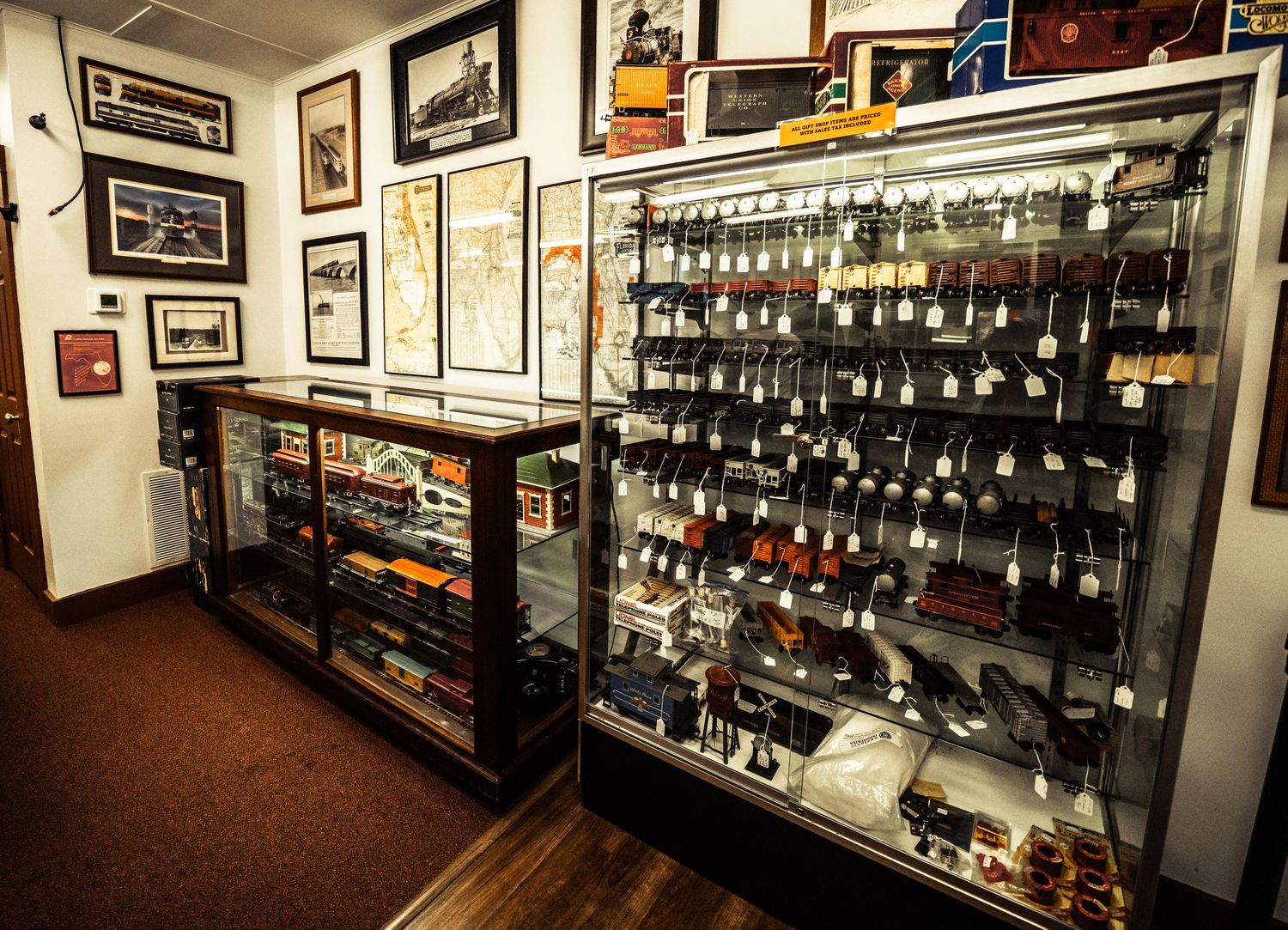 Display cases filled with model trains and railroad memorabilia line the walls of a collector's room.