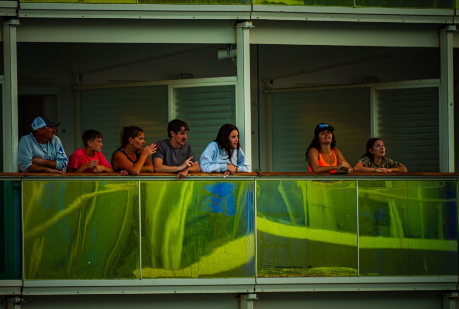 A group of people look out from a balcony with green wavy panels beneath them.
