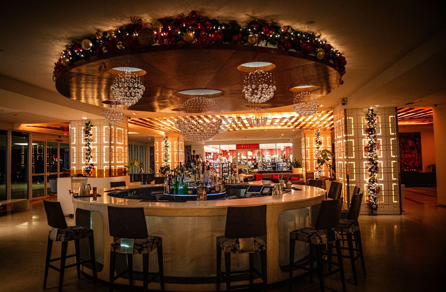 Panoramic view of a dimly lit upscale bar interior with warm lighting and elegant crystal chandeliers.
