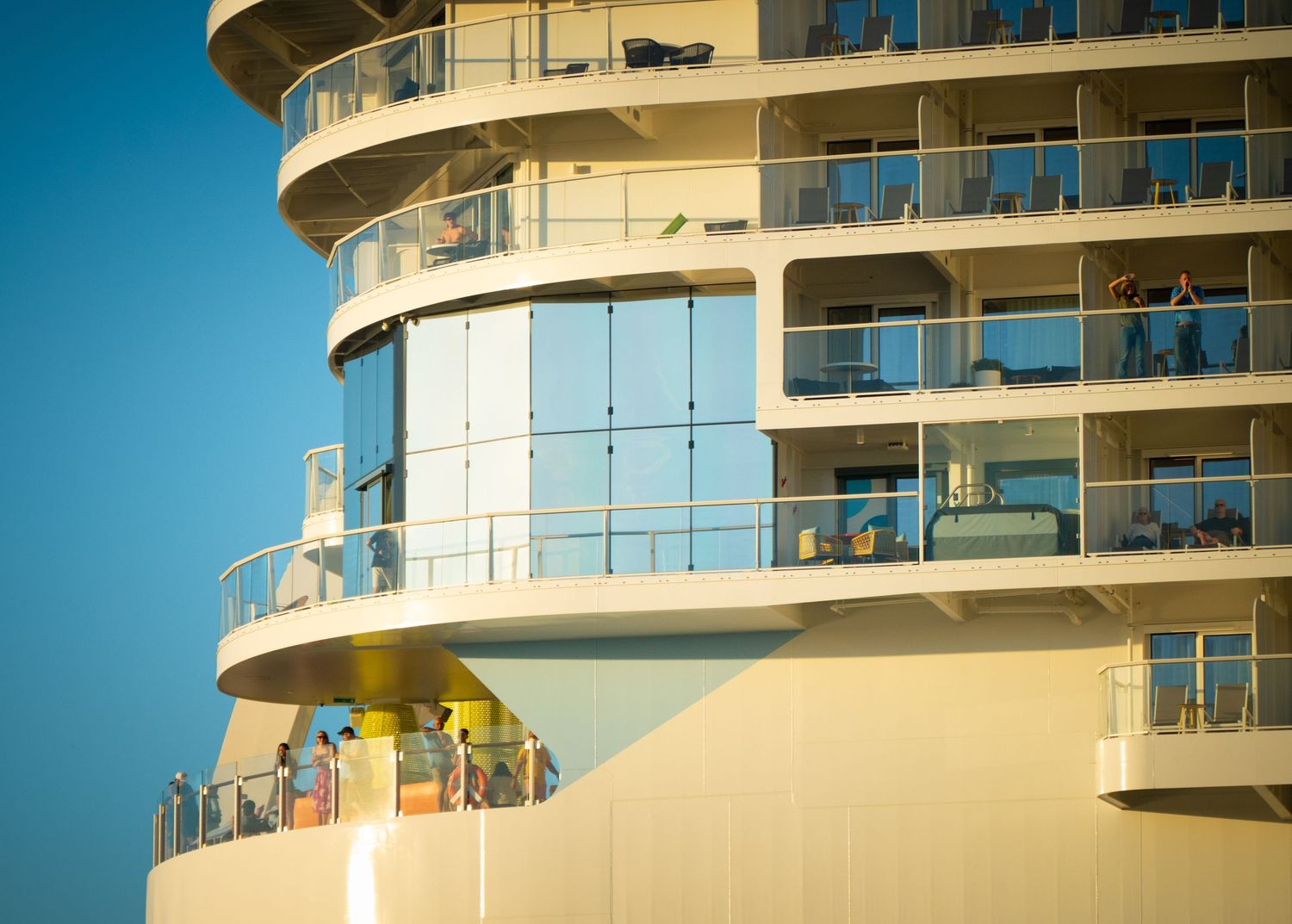 Modern luxury apartment building with curved balconies and glass railings against bright blue sky.