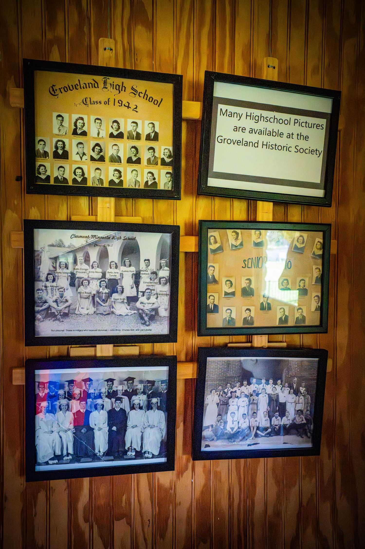 Collection of vintage class photographs and portraits displayed on wooden wall.