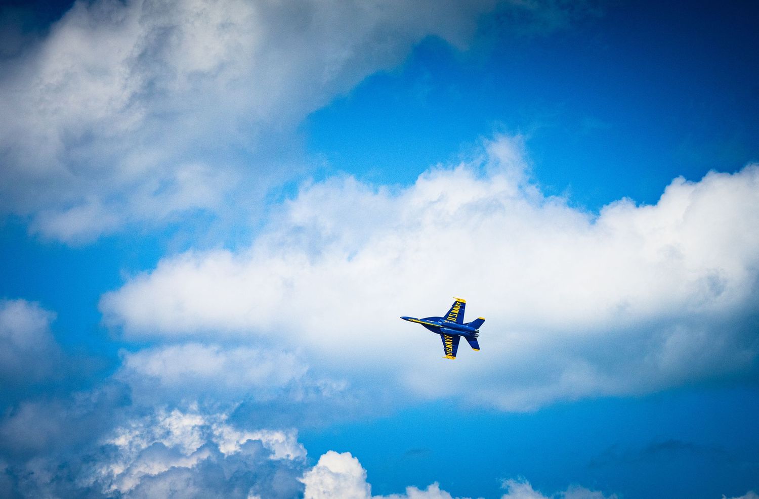 Fighter jet performs aerial maneuver against backdrop of white clouds and blue sky.
