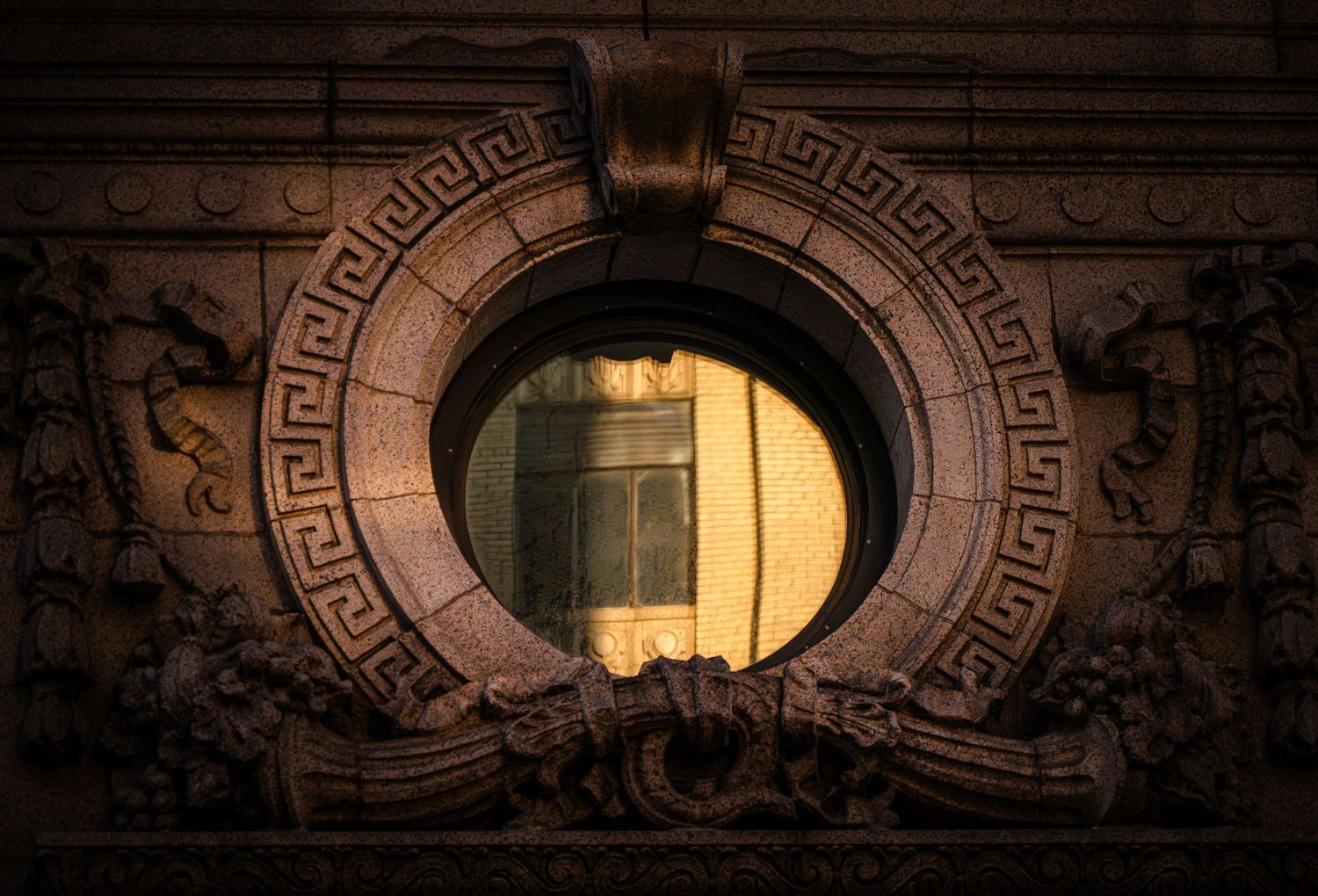 Ornate architectural detail showing Greek key pattern and arched window designs in dark lighting.