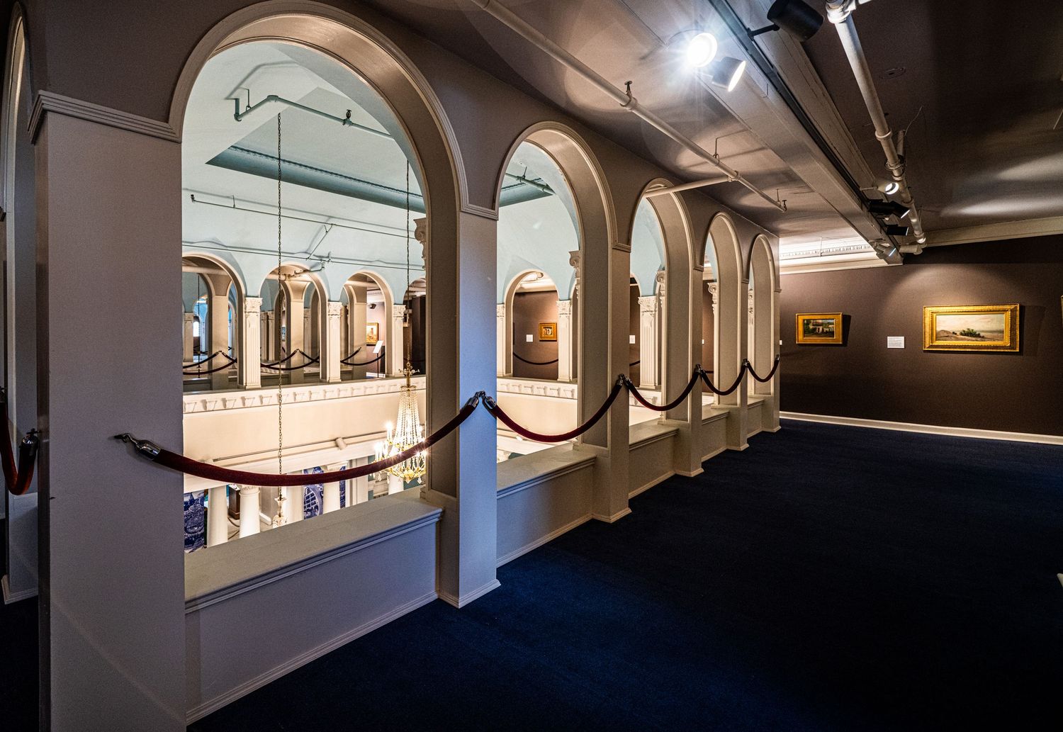 Dark museum corridor with arched windows and dramatic lighting creating atmospheric shadows.