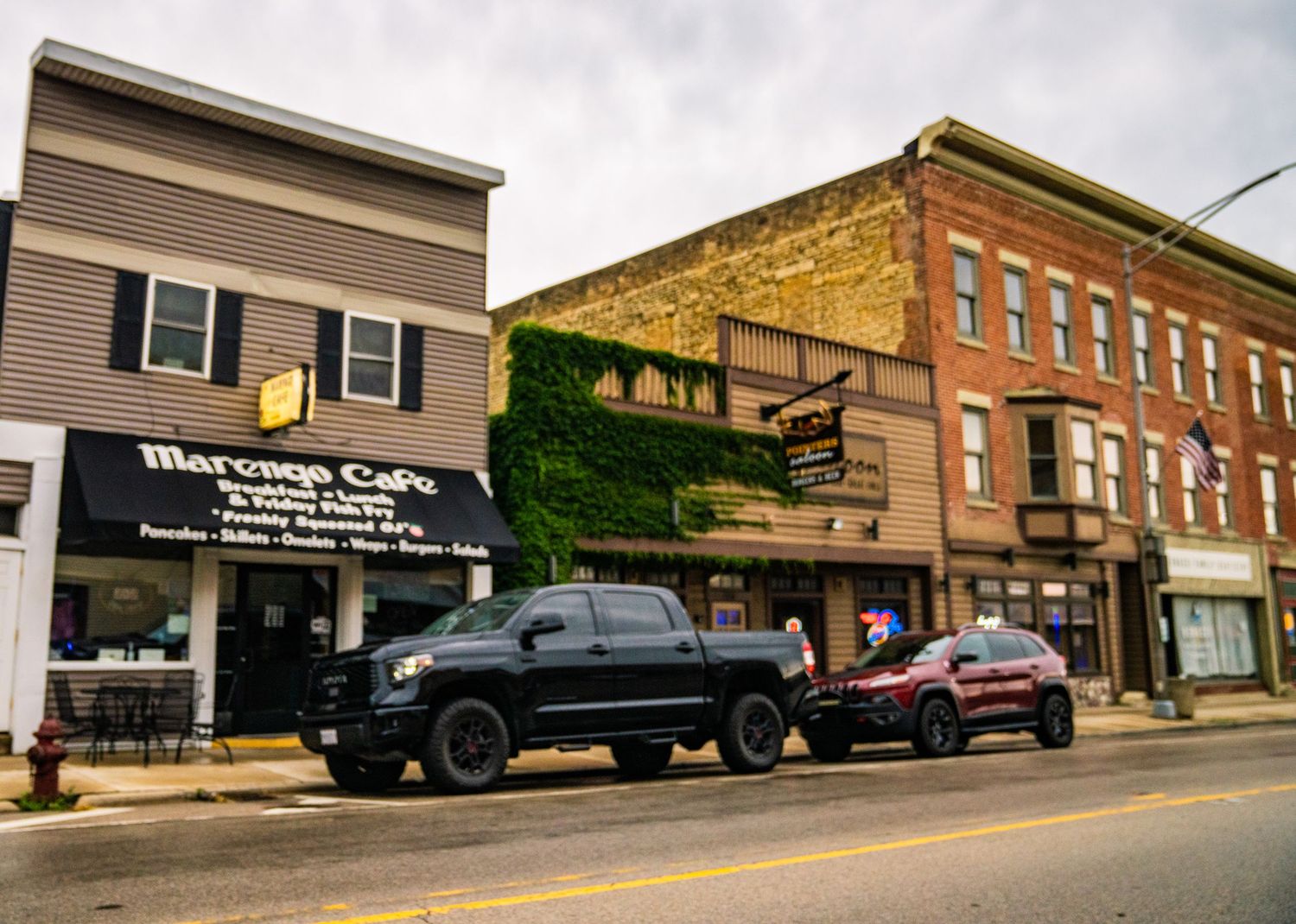 Row of vintage brick storefronts and commercial buildings on a sloped small town street.